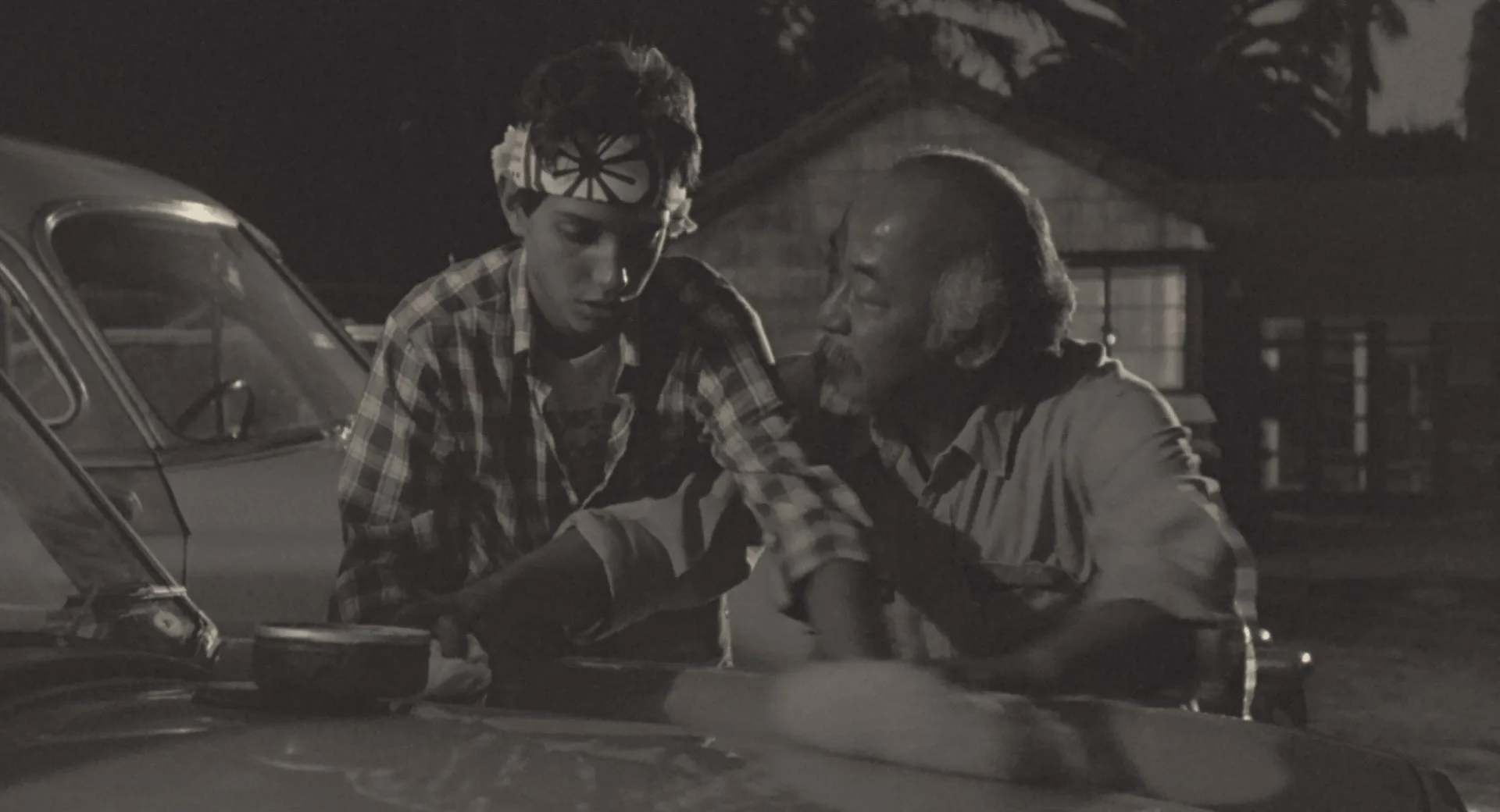Daniel and Mr. Miyagi waxing a car at dusk in The Karate Kid